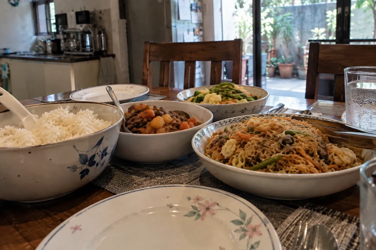 A modest home meal with rice, noodles, a main dish and vegetables set on a dining table.