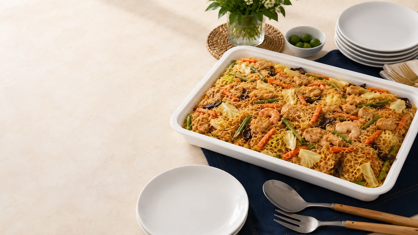 Pancit in a white rectangular party tray with serving plates arranged for quantity planning